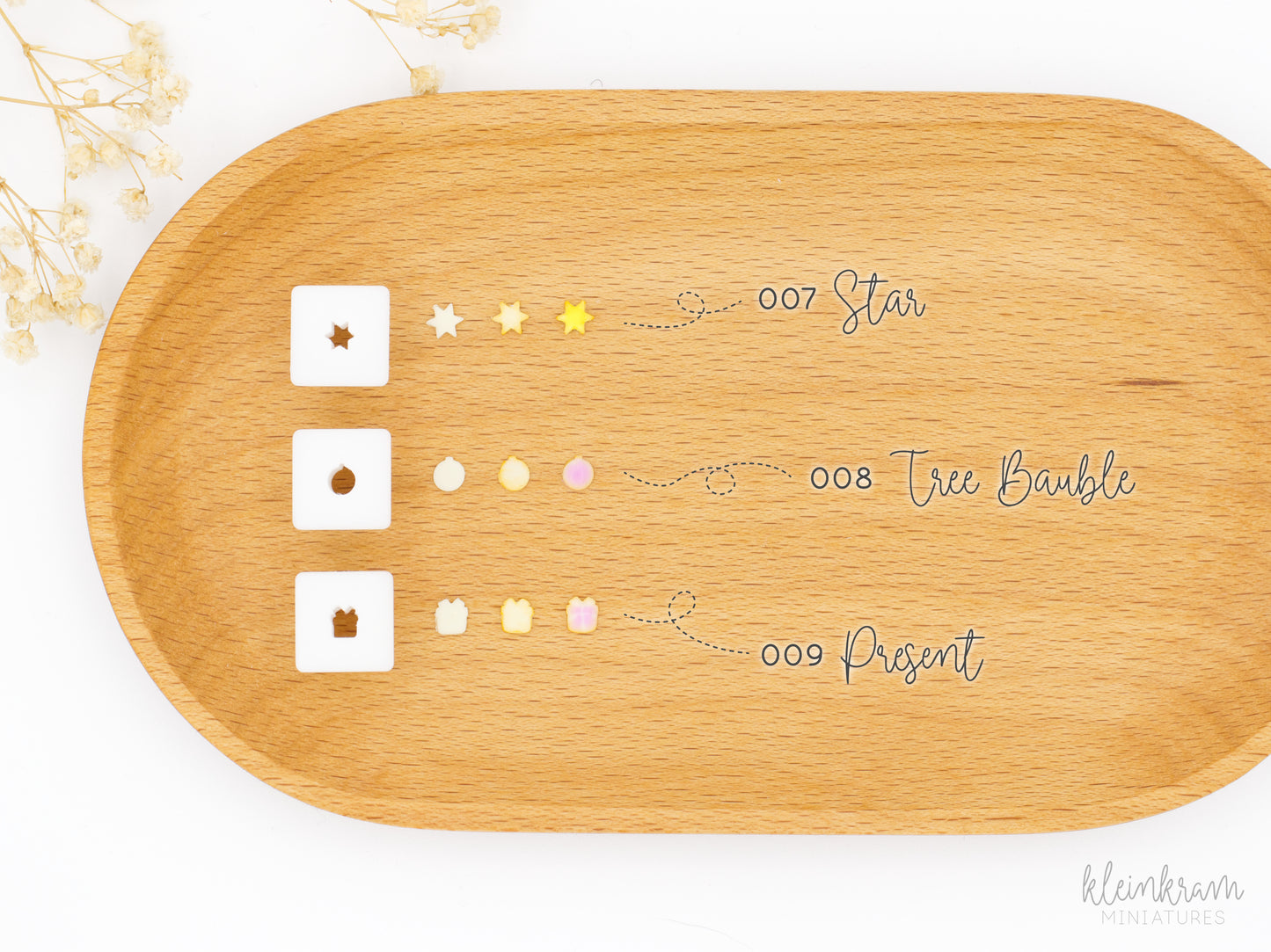 Three small square 1:12 scale clay cutters displayed next to the clay shapes they produce: a star, a tree bauble, and a present.